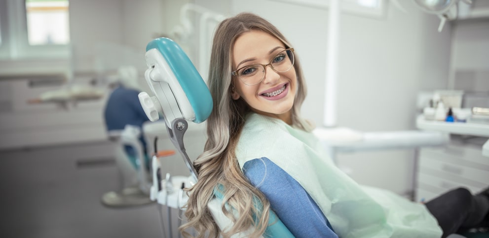 Smiling patient with braces sitting in a dental chair.