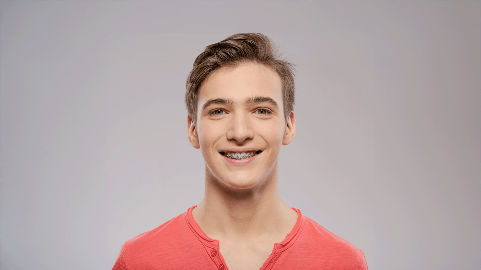 Headshot of teenager in red orange long sleeve shirt excited about his braces