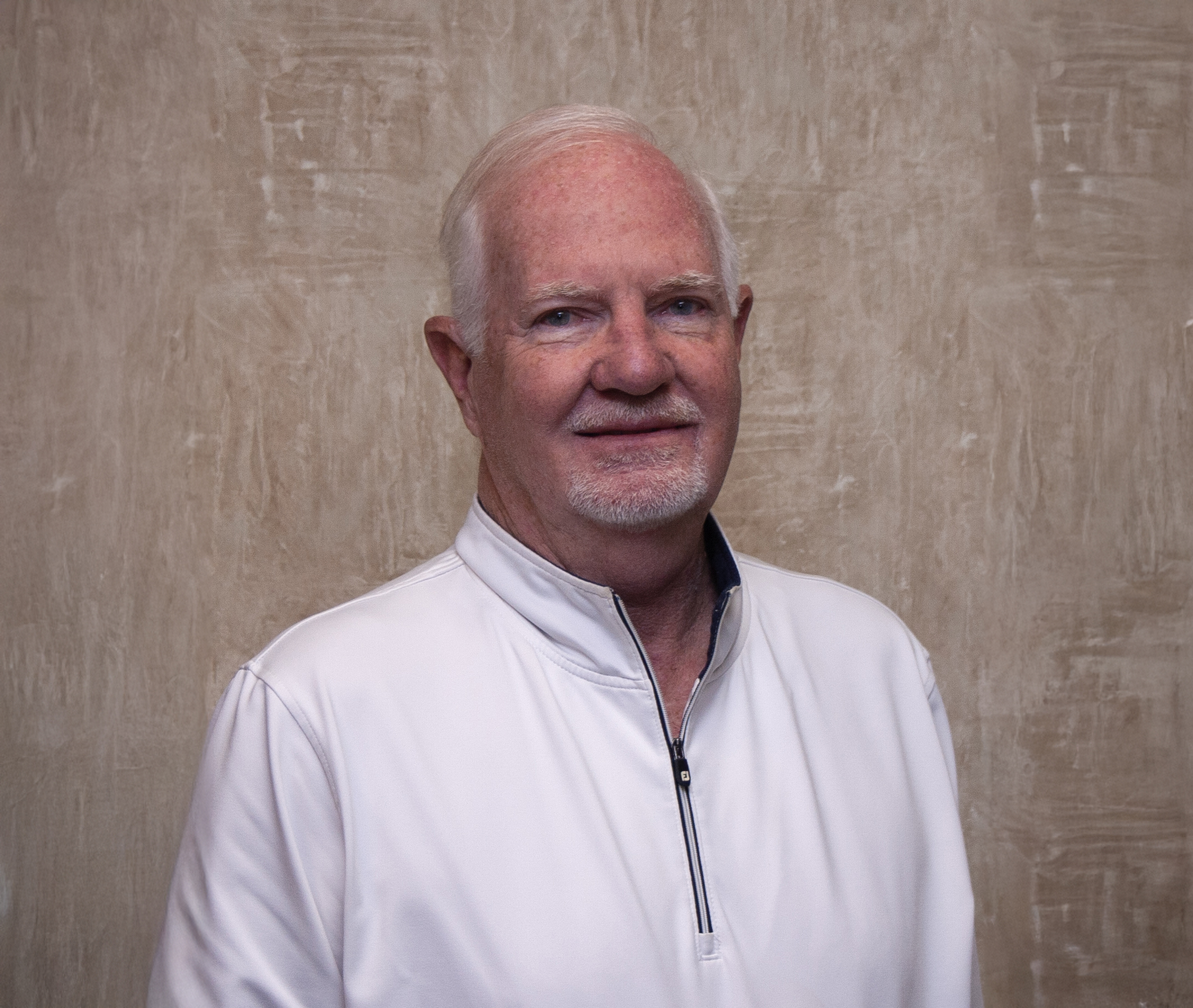 Experienced Orthodontist Dr. Koen smiling in front of a rough textured light brown wall