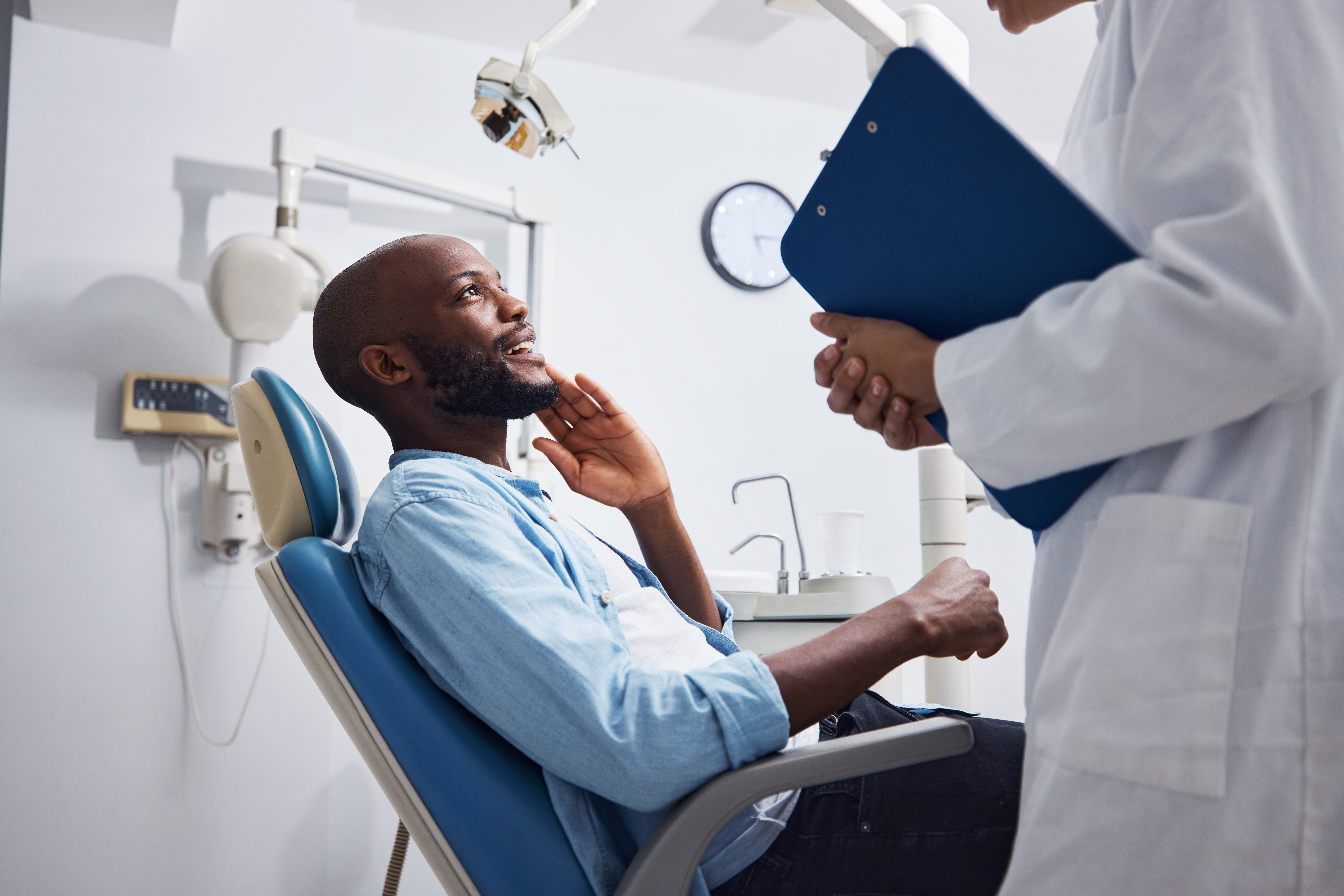An orthodontic patient sits in an orthodontist's chair and smiles at his doctor.