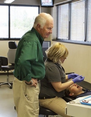 Dr. Koen looks over the shoulder of an orthodontic assistant and a boy in a treatment chair.