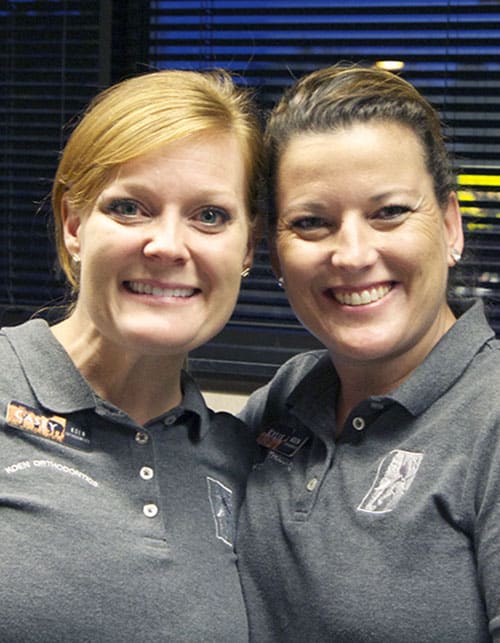 Two women smiling together in grey polo shirts.