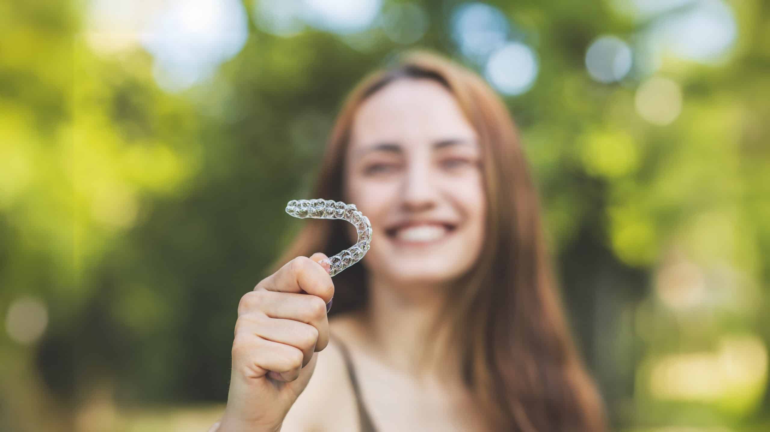 Woman in plaid holding her clear aligners on a sunny day in Hendersonville,TN