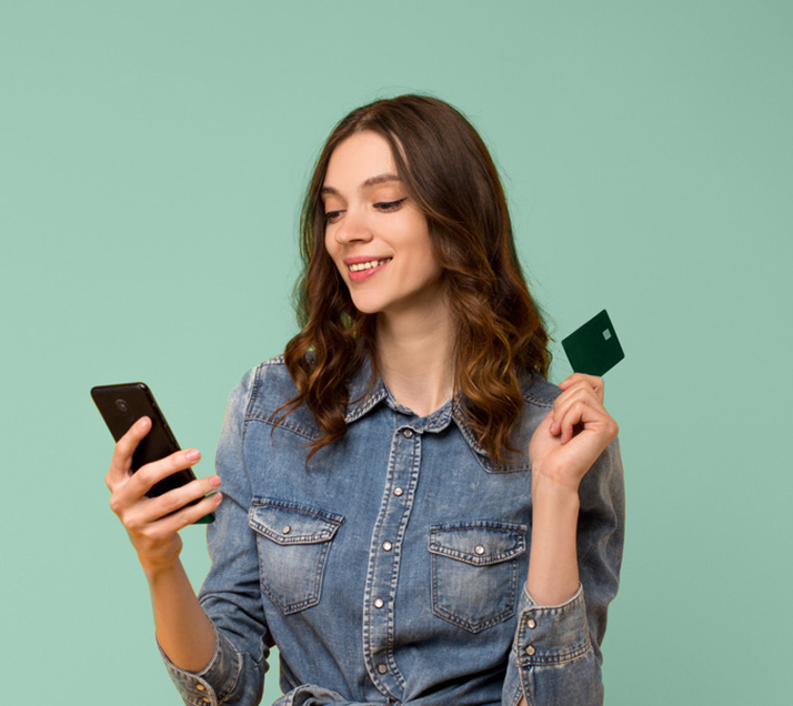 Woman in a jean jacket using her smartphone with her credit card in her other hand