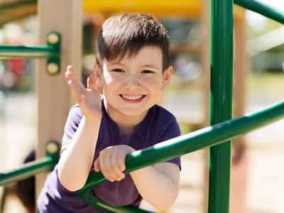 A boy smiles and waves while playing at a playground.