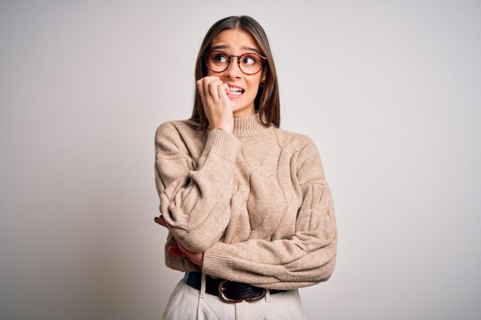 Young businesswoman wearing casual sweater looking nervous with hands on mouth biting nails