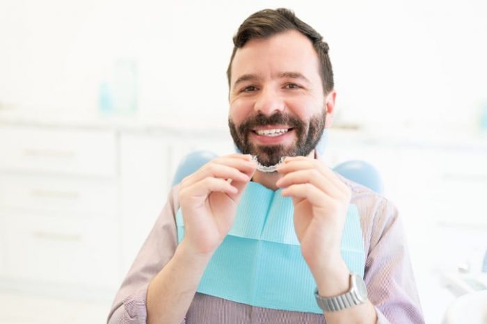 A man in a treatment chair smiling and applying a clear aligner to his teeth.