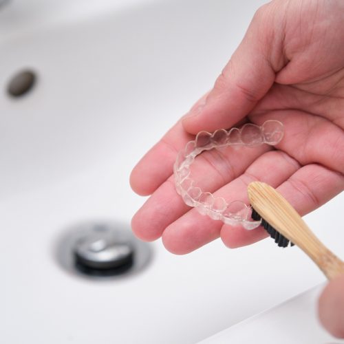 an orthodontist patient cleaning their invisalign with a toothbrush over the sink