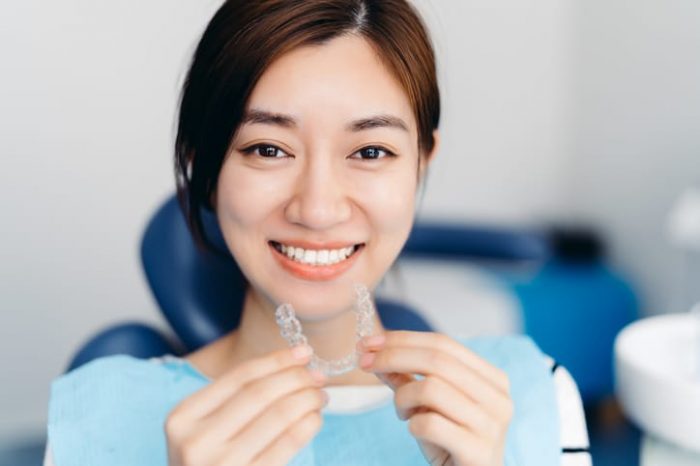 A girl smiling and holding a clear aligner.