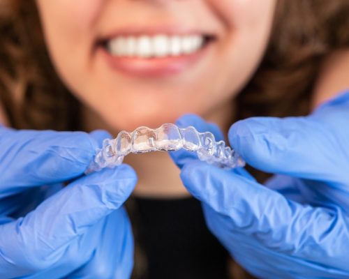 an orthodontist using blue dental gloves to insert invisalign aligners in a female patients mouth