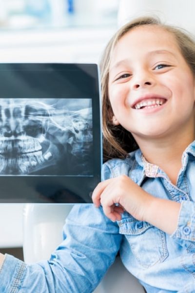 Girl at the dentist holding and x-ray and looking at the camera smiling