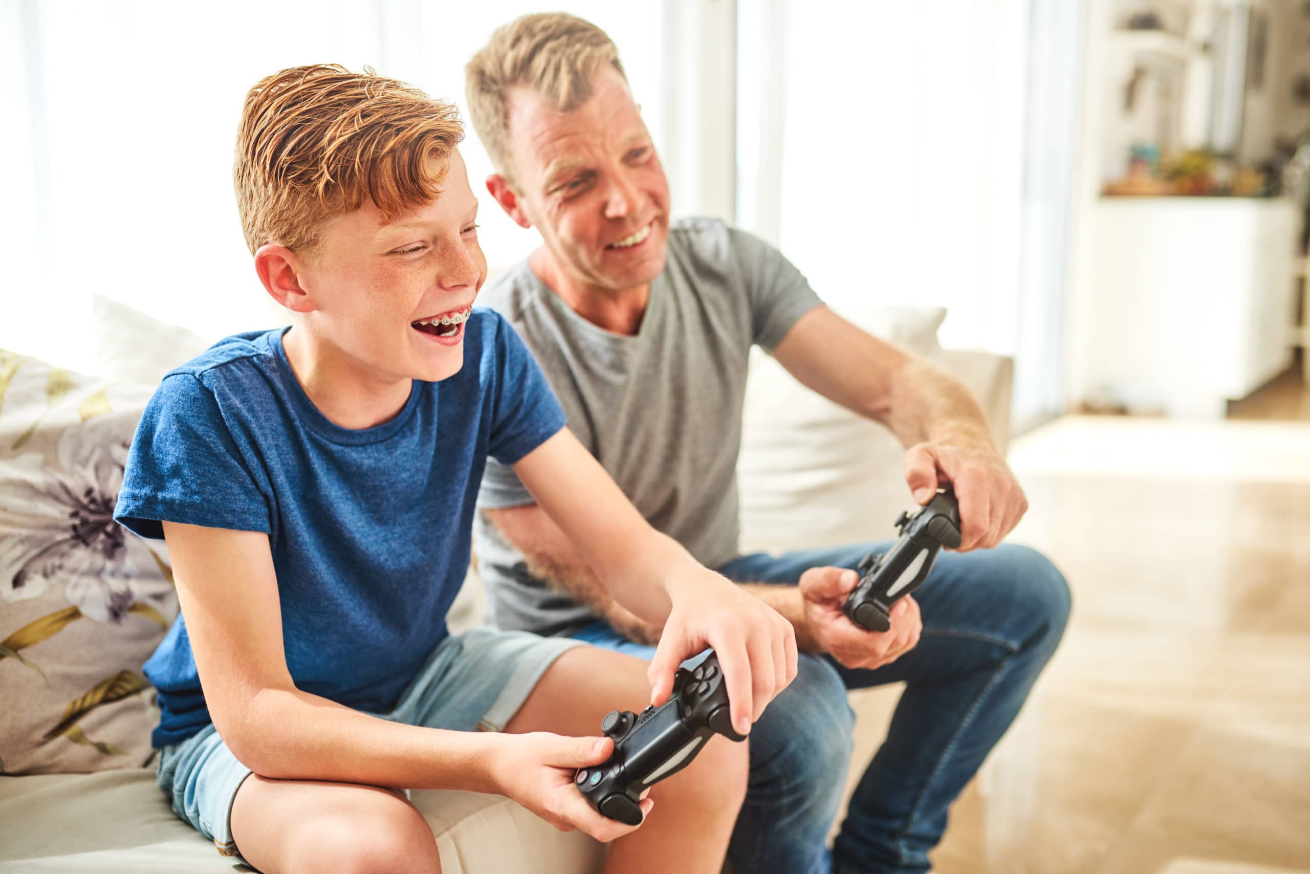 A young boy with braces playing video games with his dad.