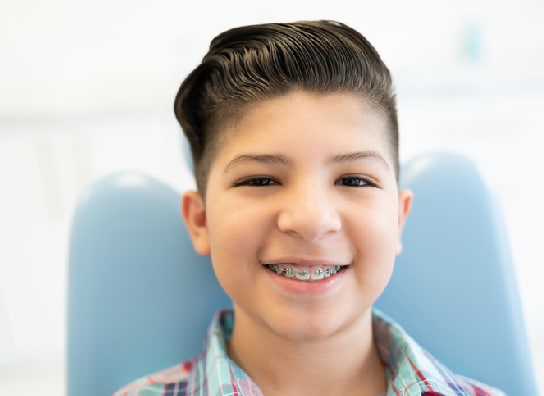 A smiling boy with green metal braces sitting in a treatment chair.