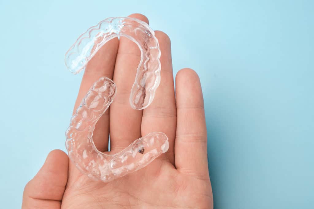 A hand holding two clear aligners.