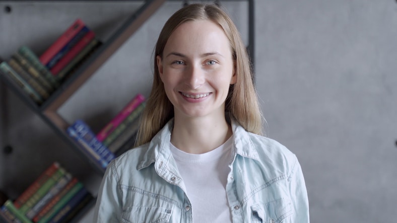 A smiling girl standing in front of a bookcase.