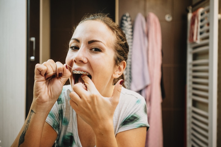 A woman with braces looking in the mirror while she flosses her teeth