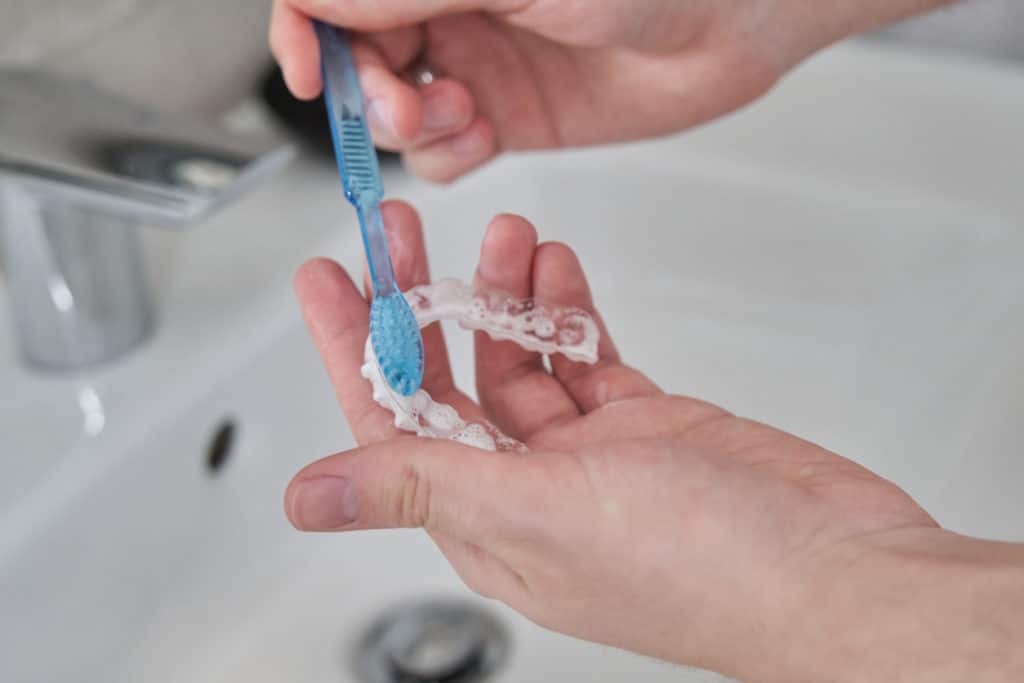 a person cleaning their invisalign clear aligners with a toothbrush