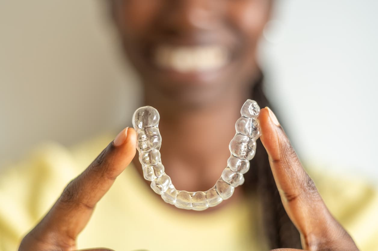 Young woman in a yellow top holding her invisalign tray with her her two index fingers