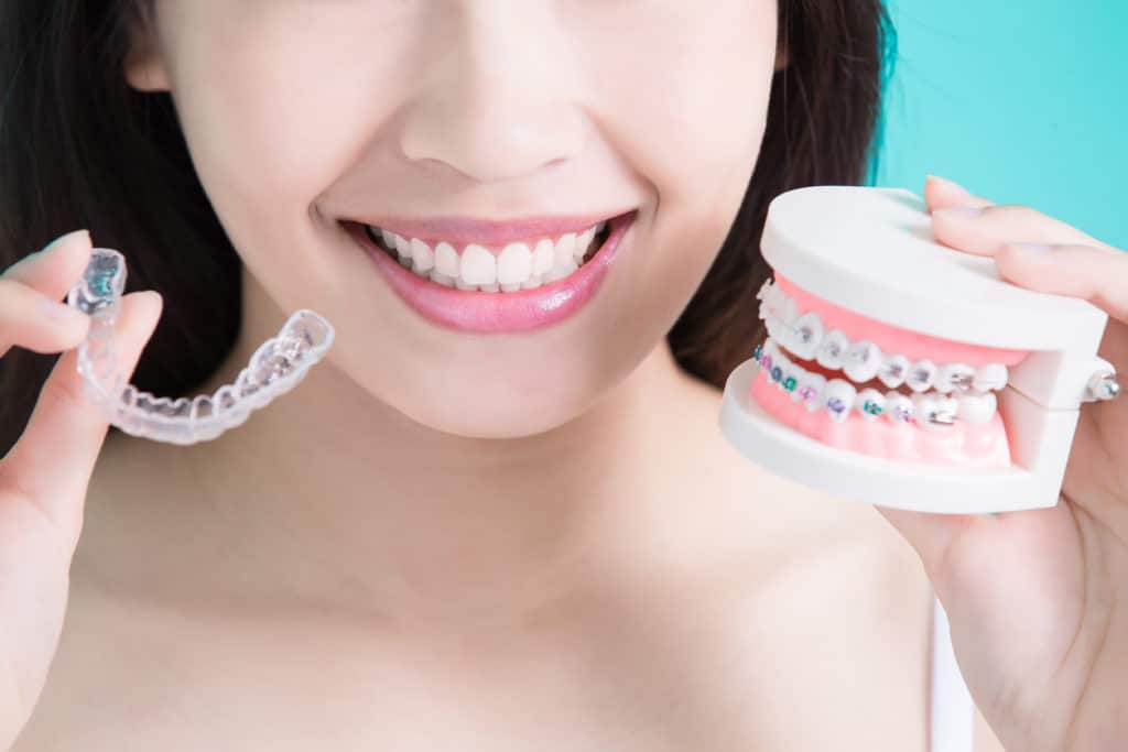 a woman holding a dental typodont and invisalign clear aligners