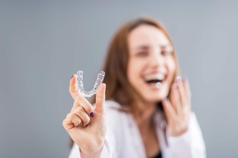 a happy woman holding her invisalign clear aligner